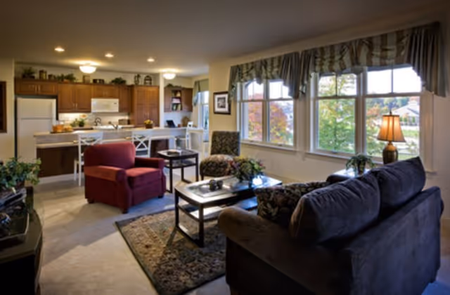 Open-plan living room with sofa, armchair, coffee table, and a kitchen with a breakfast bar visible in the background.