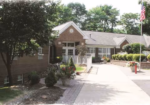 Front exterior of a brick senior living facility with walkway and flag.