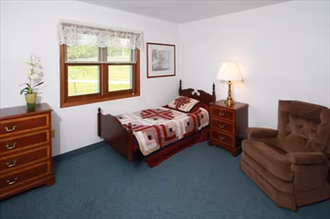 A furnished bedroom with a bed, nightstands, dresser, lamp, and a brown recliner chair.
