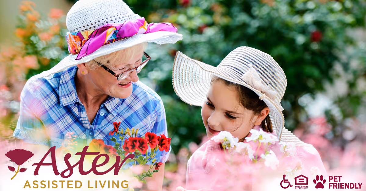 An elderly woman and a young girl wearing sun hats are enjoying time together in a garden surrounded by colorful flowers. The elderly woman is smiling and looking at the girl, who is also smiling and looking at the flowers.