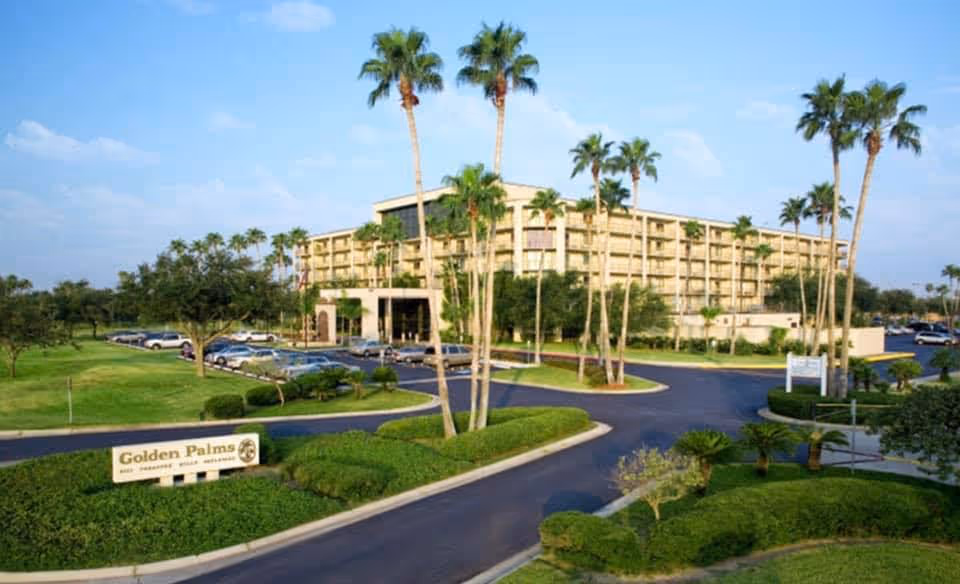 Entrance view of a multi-story retirement complex surrounded by palm trees, lawns, a circular driveway, and a sign reading "Golden Palms".