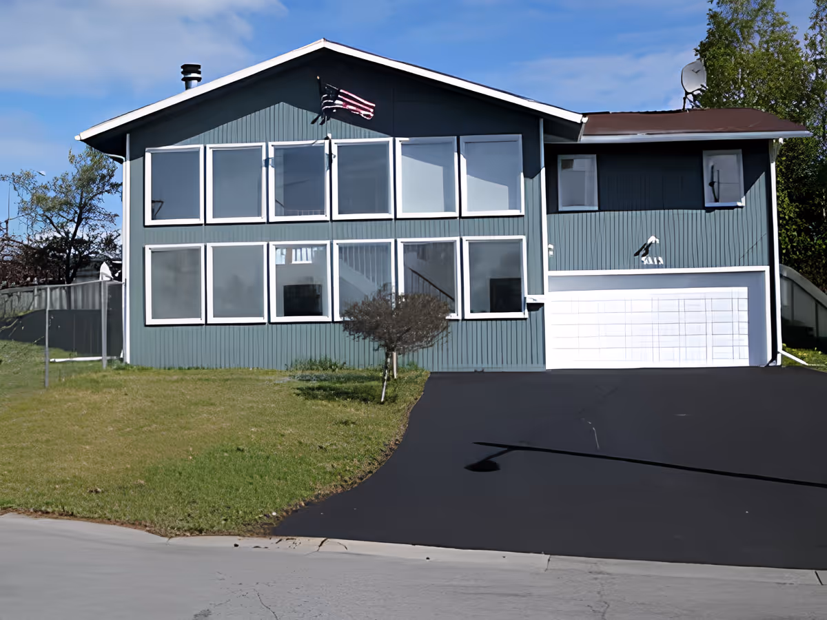 Front exterior of a two-story house with large windows, a white garage door, an American flag, and a paved driveway.