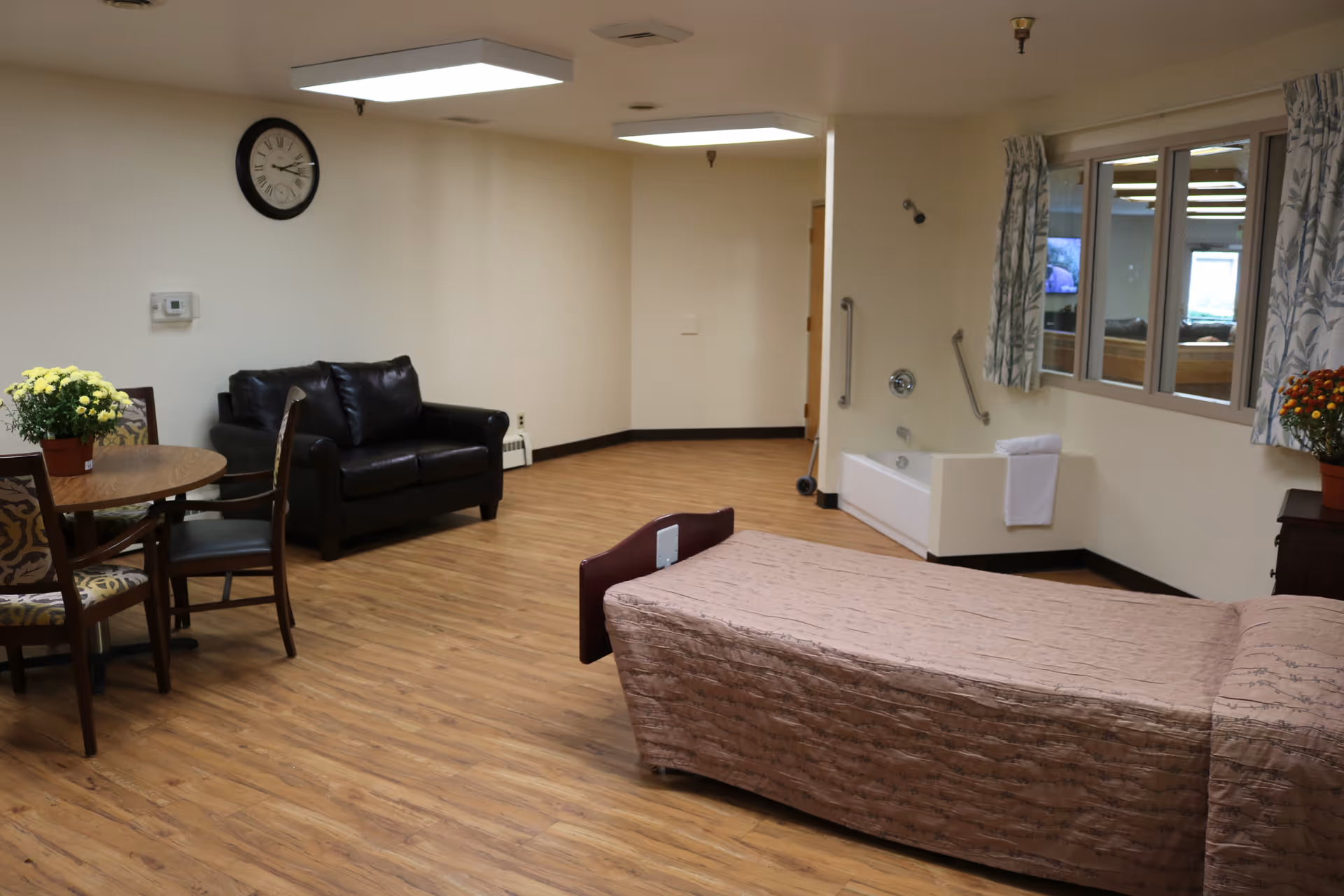 Spacious senior living resident room with a bed, seating area, dining table, and an accessible bathtub.