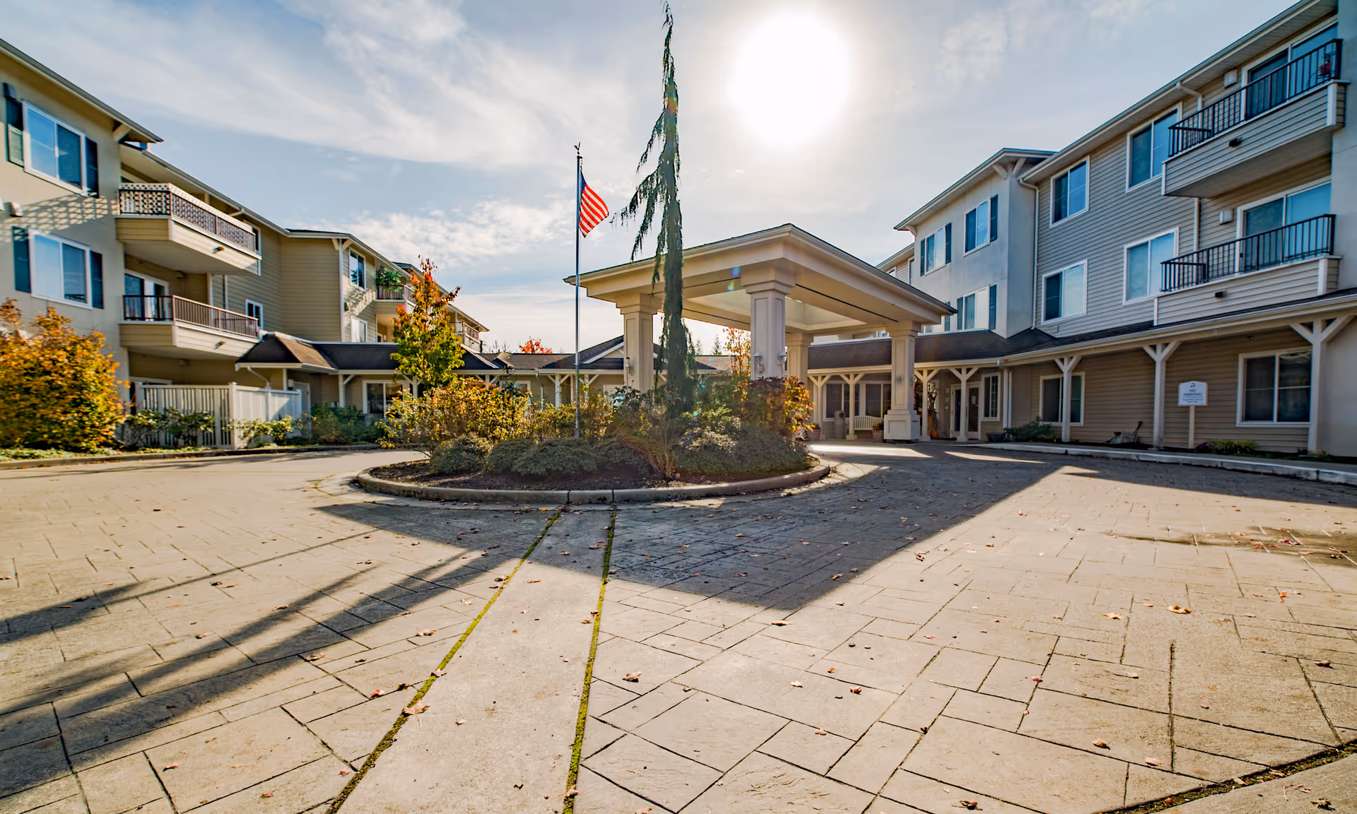 Front entrance and covered portico of a multi-story senior living building with a circular driveway and an American flag.