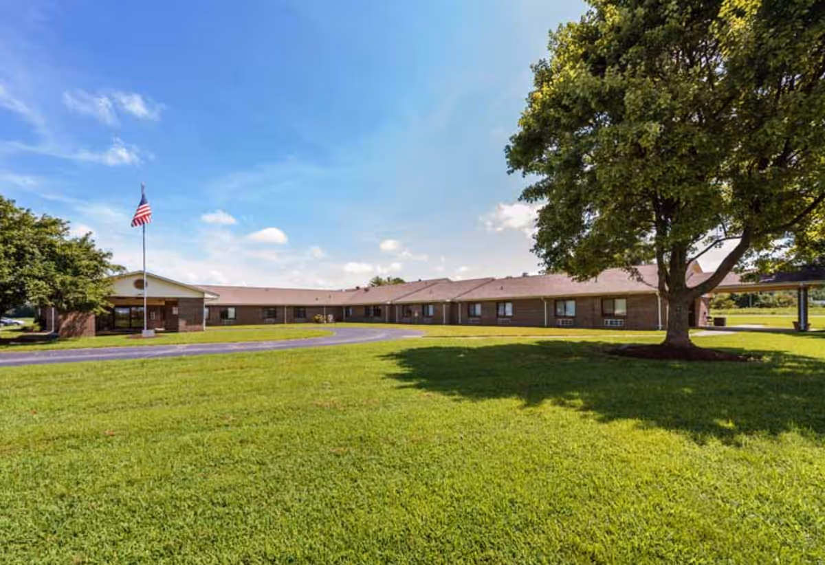 Single-story brick senior living facility with flagpole, expansive lawn, and large tree.