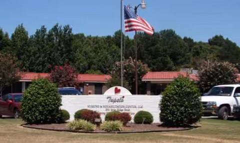 Front entrance sign for Tupelo Nursing and Rehab Center with flag and shrubs.