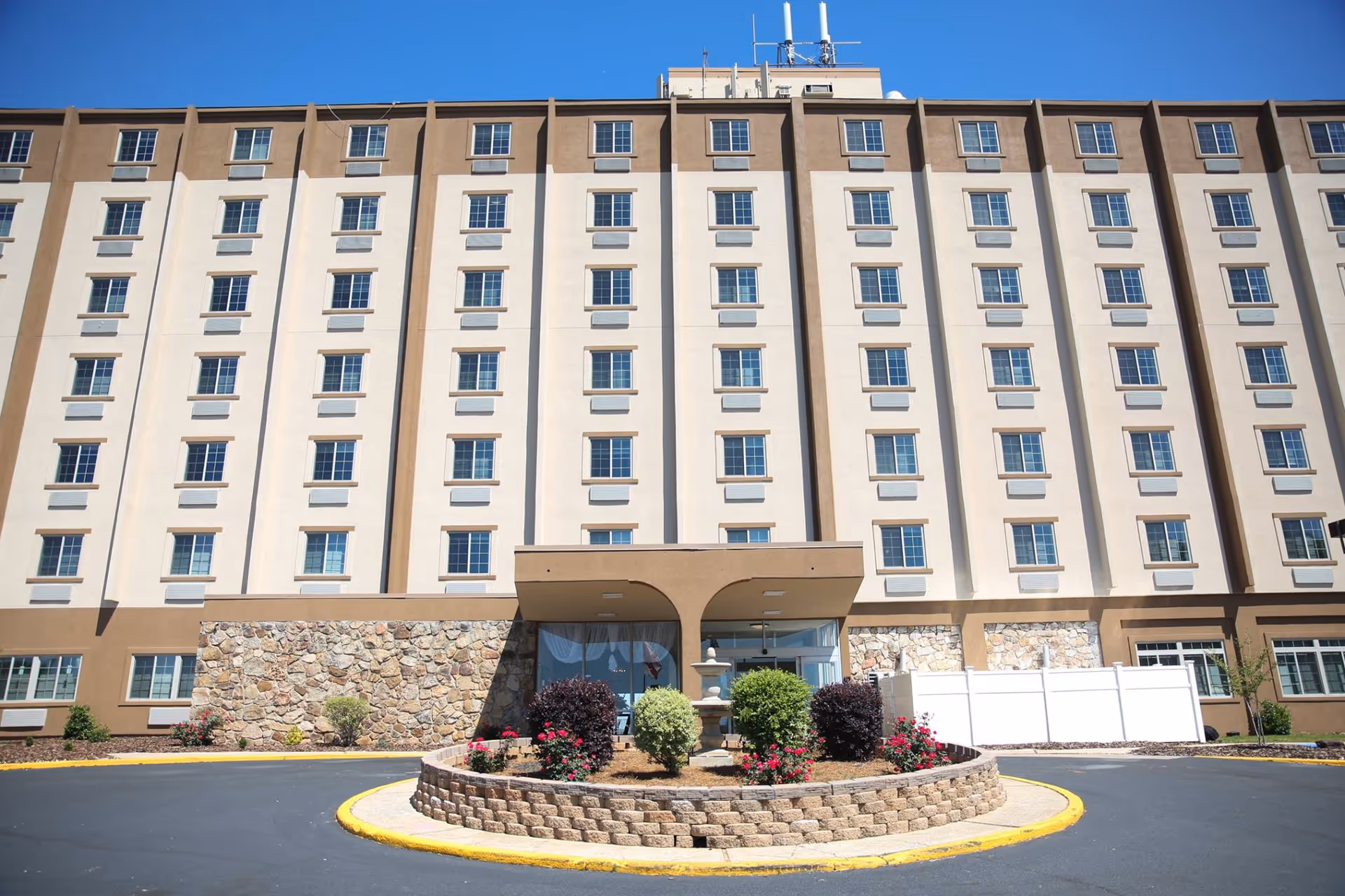 A tall beige senior living building with a circular driveway and landscaped entrance.