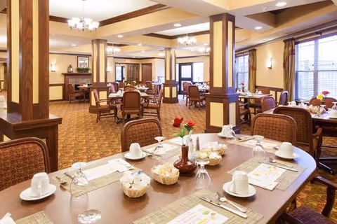 Bright, spacious senior dining room with multiple set tables, warm wood columns and chandeliers.
