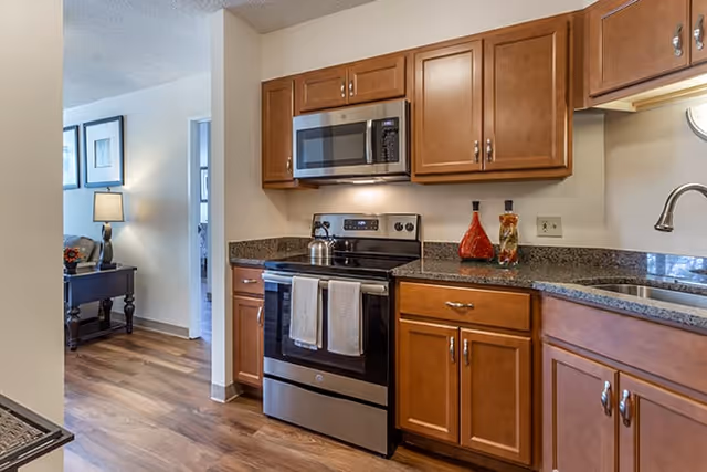Open-plan kitchen with stainless steel stove and microwave, wooden cabinets, granite countertops and hardwood floors.