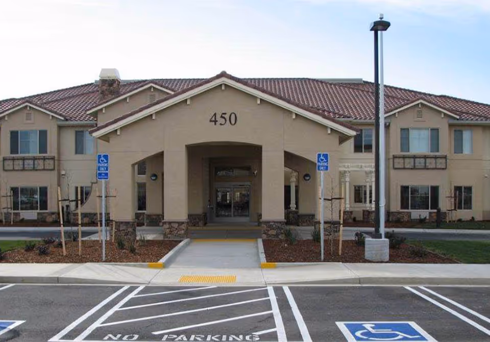 Front entrance of a beige two-story senior living building labeled "450" with a covered drive-up entry and accessible parking spaces in front.