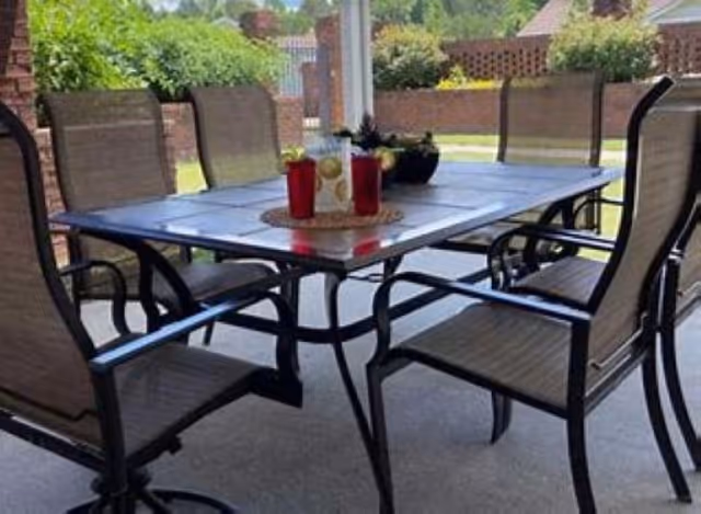 Patio dining table with metal-framed chairs set on a covered outdoor patio overlooking a yard.