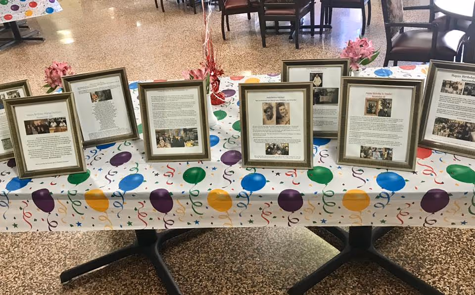 A long table in a dining area covered with a balloon-patterned tablecloth displaying several framed photos and documents.