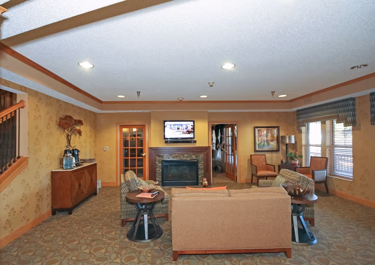 Cozy communal living room with sofas and chairs arranged around a fireplace and wall-mounted TV.