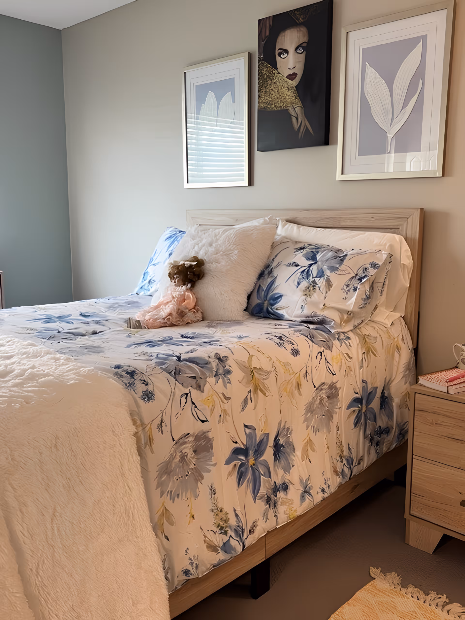 A neatly made bedroom with a floral-patterned bed, decorative pillows and framed artwork above the headboard.