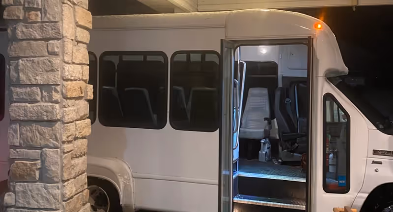 White shuttle bus is parked beside a stone building with an open door at night.