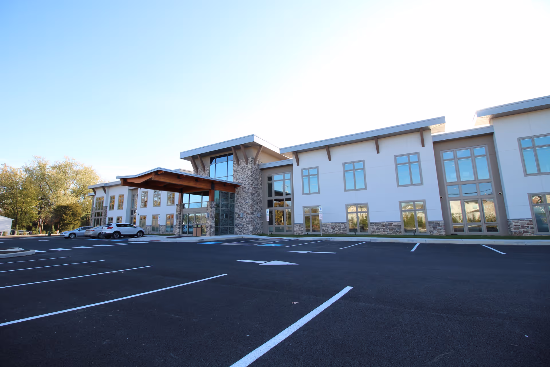 Front exterior of a modern two-story senior living building with large windows and an empty parking lot.