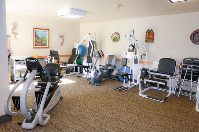 A bright exercise room with several cardio and strength-training machines and fitness equipment.