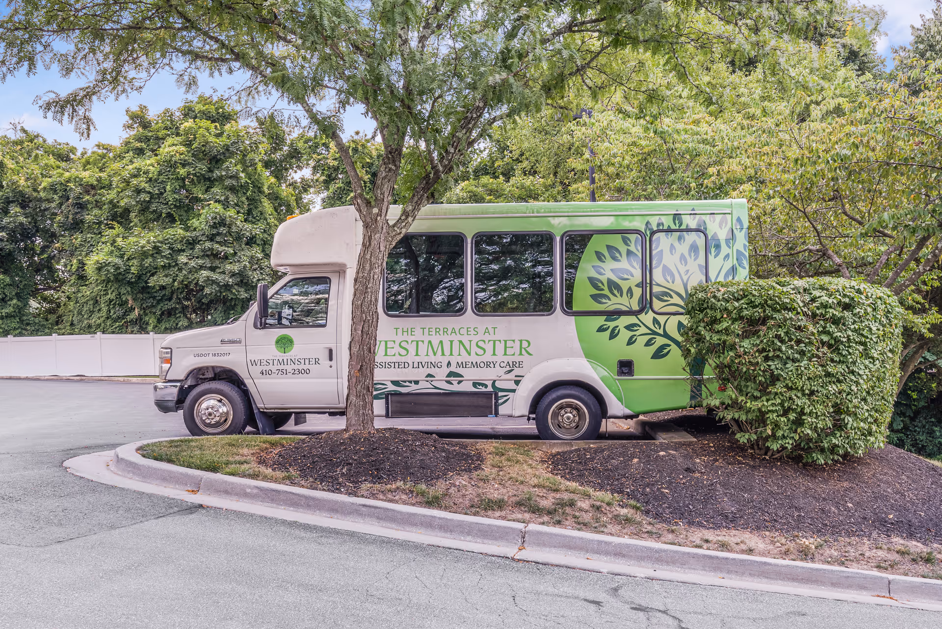 A green-and-white shuttle bus labeled 'The Terraces at Westminster' parked near trees and shrubs.