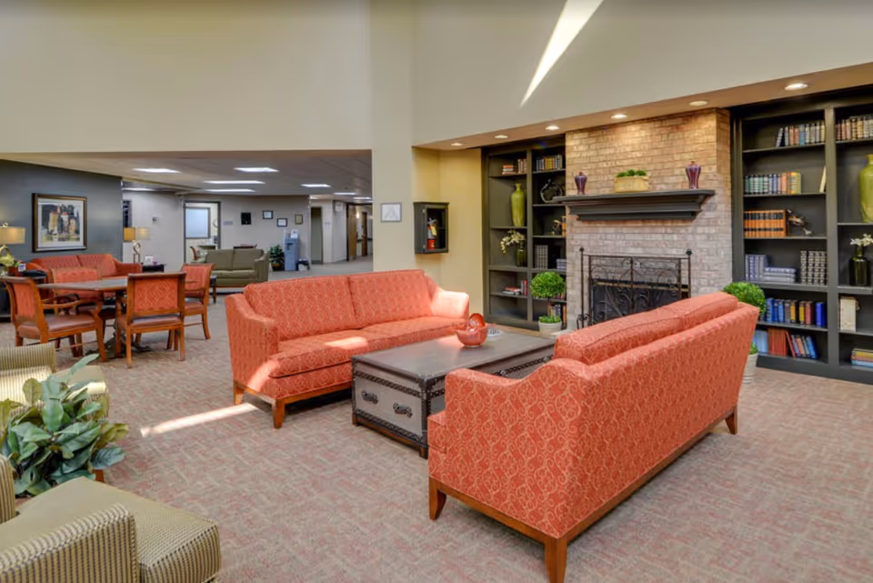 Communal lounge with red patterned sofas arranged around a coffee table in front of a brick fireplace and built-in bookshelves.