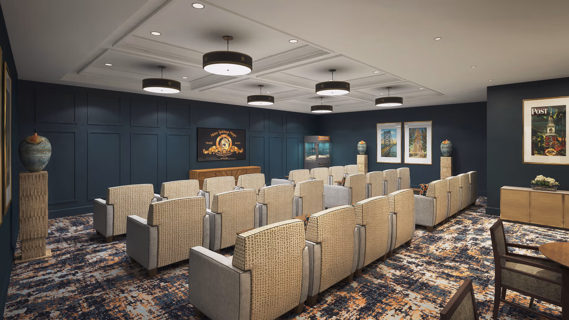 A cozy interior screening room with multiple rows of upholstered armchairs facing a dark paneled wall with framed artwork and pendant lights.