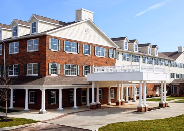 Three-story brick and beige-sided senior living building with many windows and a white columned covered entrance.