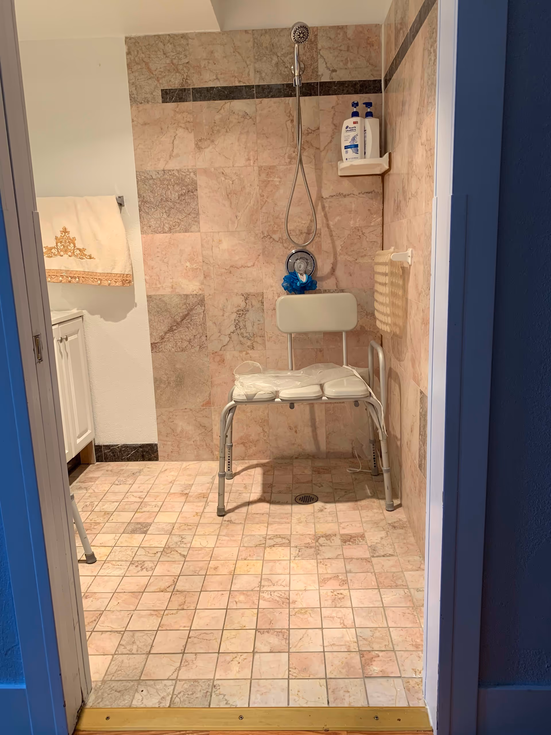 Tiled walk-in shower with a padded shower chair, handheld showerhead, and mounted toiletries.