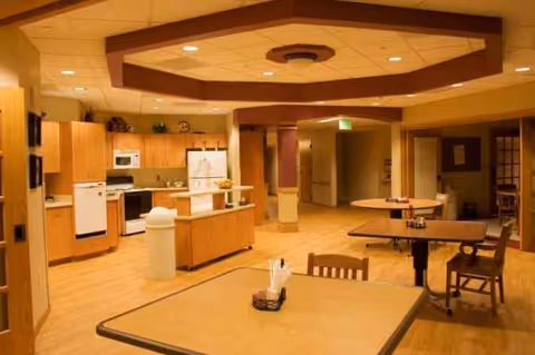 Indoor communal dining area with wooden tables, chairs, and a visible kitchen in the background.