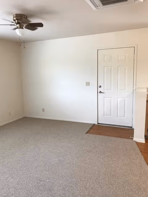 Empty room with beige carpet, white walls, a white door, and a ceiling fan with light fixture.