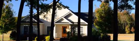Front exterior of a single-story senior living facility with trees and a covered entry porch.