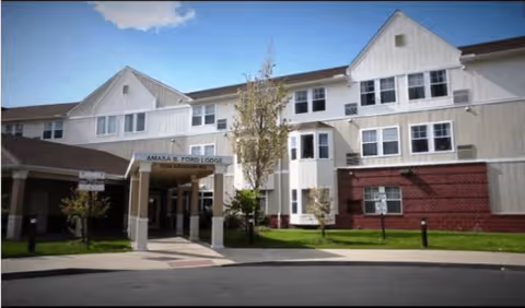 Exterior view of a senior living center with a covered entrance and trees.