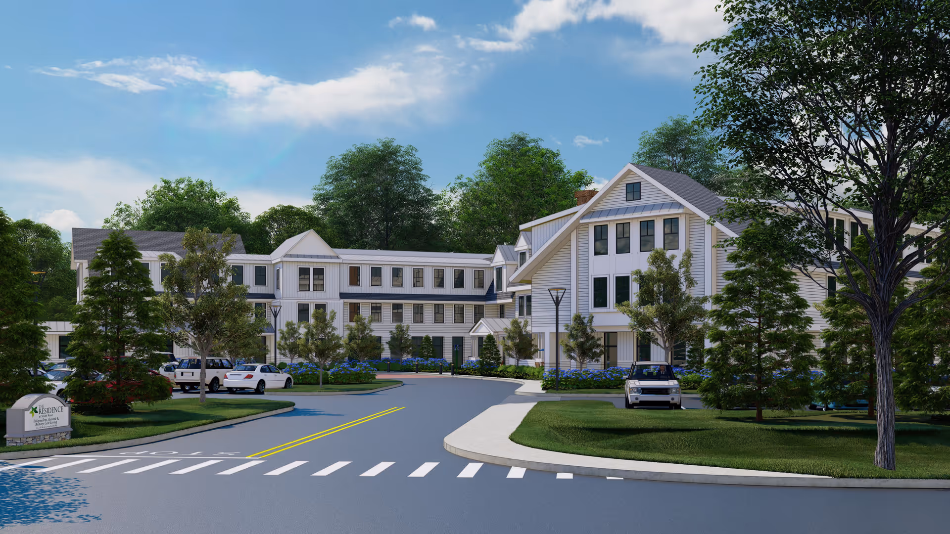 Exterior view of The Residence at Bedford, a multi-story senior living facility surrounded by trees and landscaped greenery, with a driveway and parked cars in front under a partly cloudy sky.