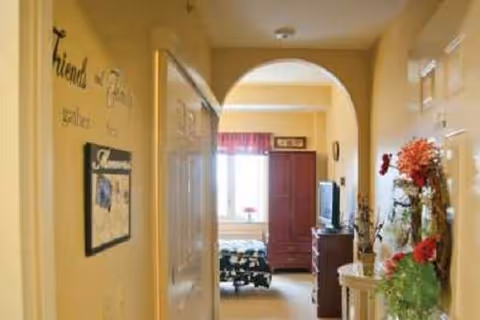 Decorated hallway with an arched doorway opening into a bedroom containing a bed, armoire and television.