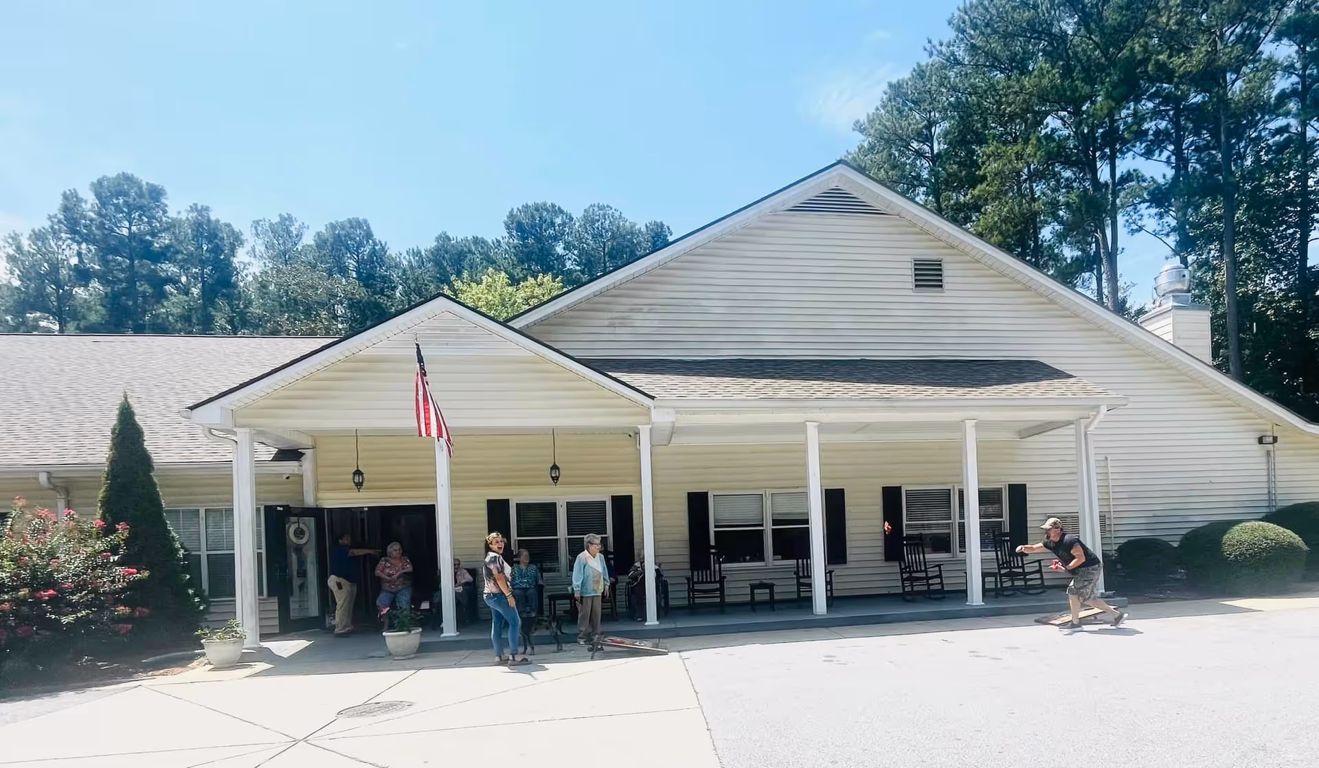 Exterior of Bountiful Hills Senior Living Community with porch, flag, and residents outside.