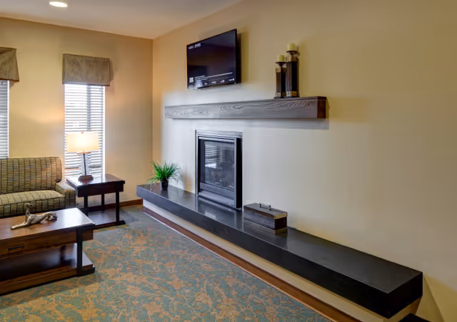 Living room with a couch, coffee table, fireplace beneath a wall-mounted TV and a long black shelf.