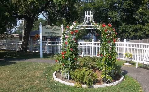 Outdoor garden with a circular flower bed arch, white fence, and Locust Lodge sign.