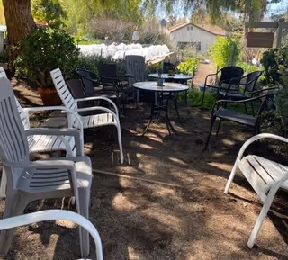 Shaded outdoor seating area with plastic chairs and small tables arranged in a garden courtyard.
