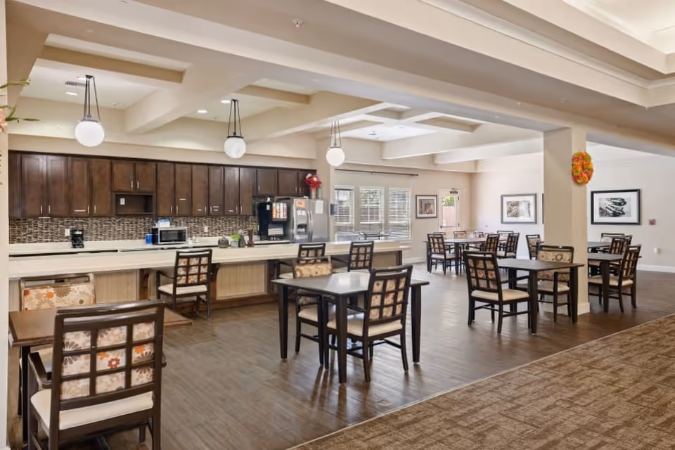 Spacious communal dining room with multiple tables and chairs and a long kitchen counter with cabinets and appliances.