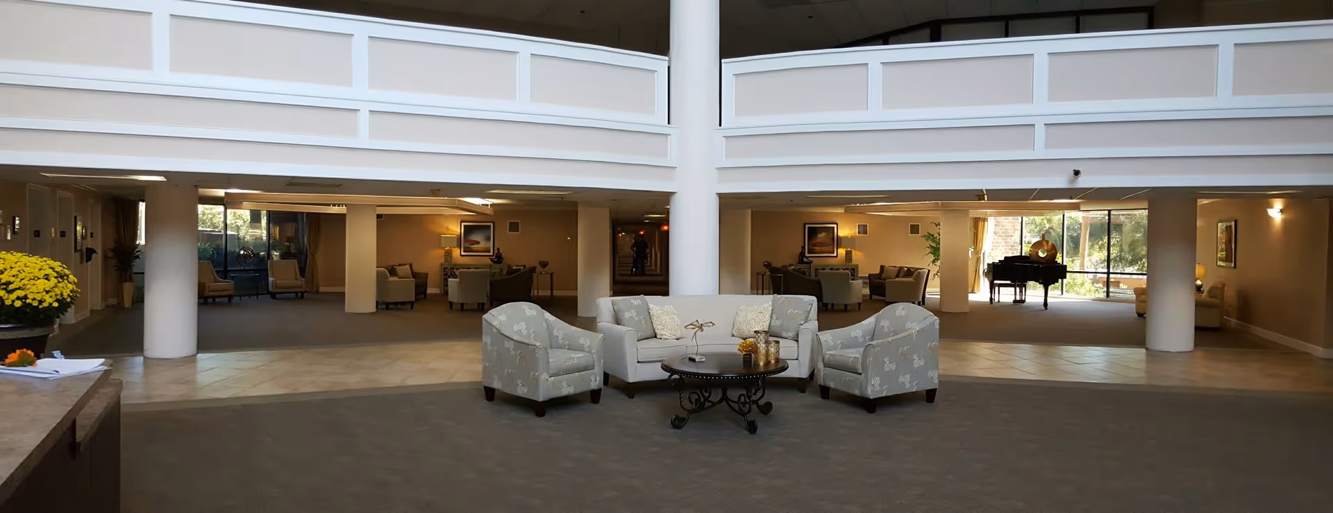 Spacious lobby of Hampton Apartments with a central seating arrangement, surrounding lounge areas, and a grand piano beneath an upper balcony.