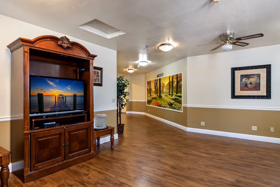Spacious common area with a wooden TV cabinet, wall art, hardwood floors, and ceiling fans.