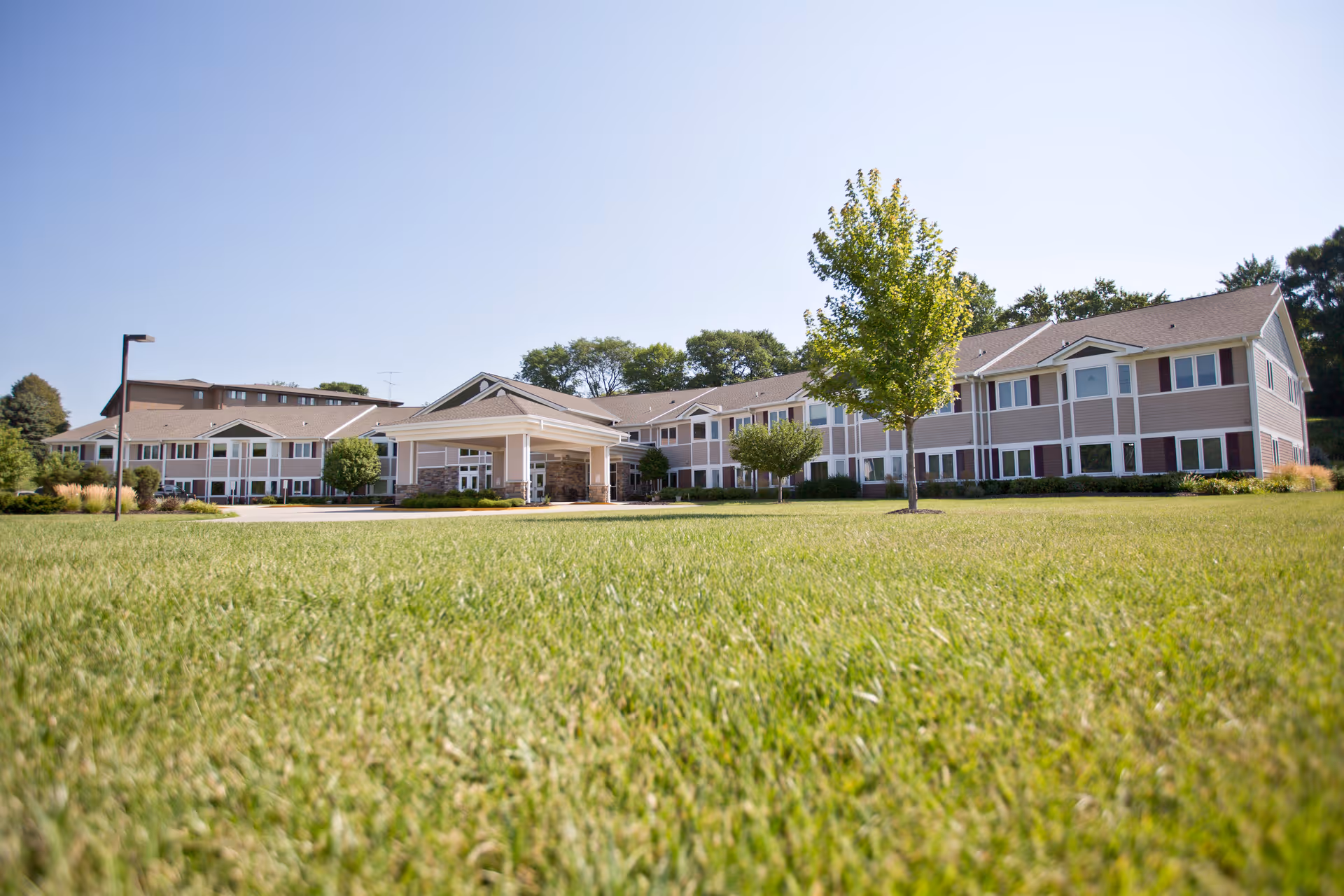 Wide view of Silveridge Assisted Living, An Eventide Community building with a large green lawn in the foreground, a few trees, and a clear blue sky.