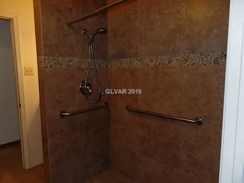 Tiled walk-in shower with grab bars and a handheld showerhead.