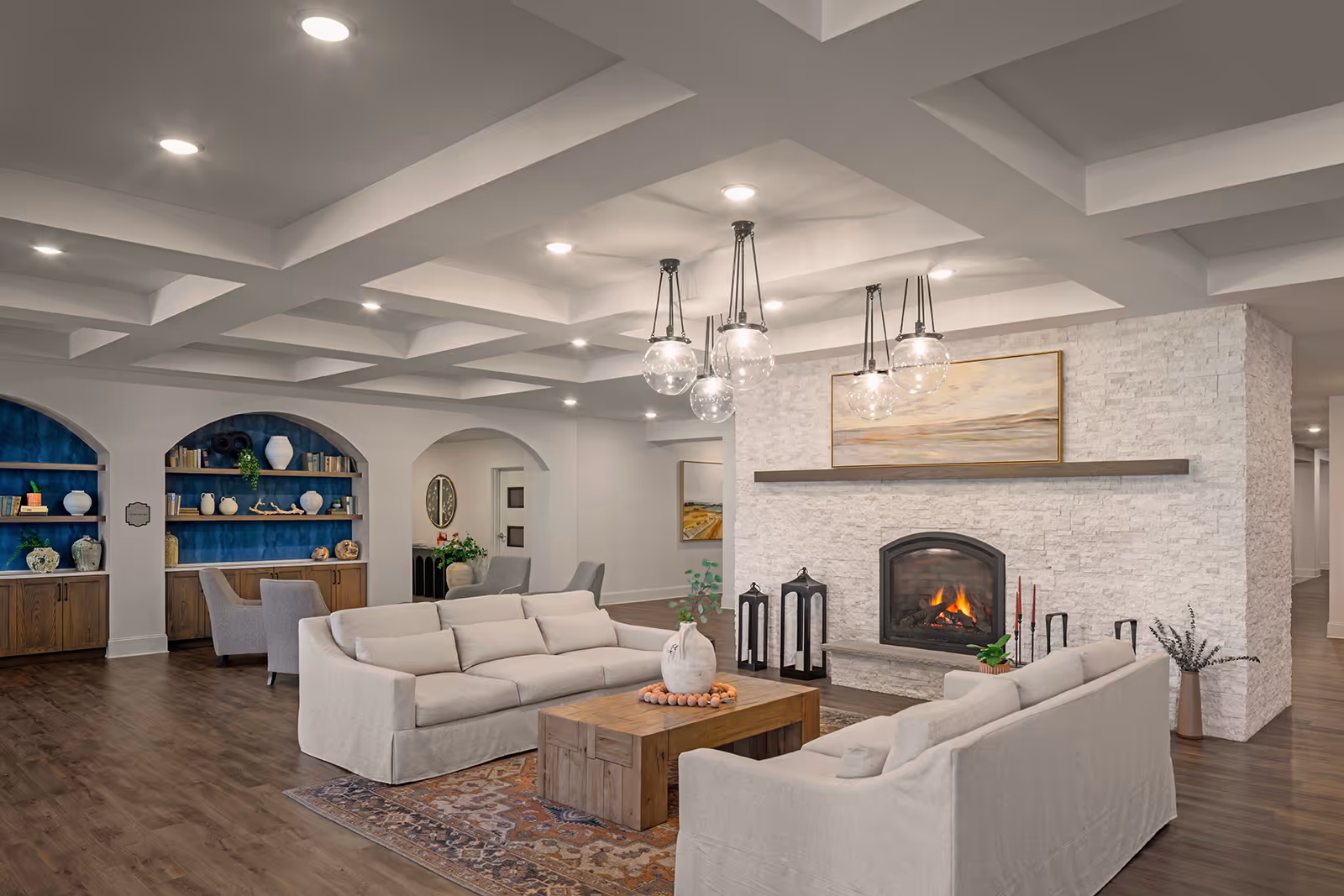 Spacious modern common lounge with cream sofas and a wooden coffee table facing a stone fireplace beneath pendant lights.