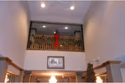 Interior view of a two-story living area decorated for Christmas with a garland and a large red bow on the upper railing, a framed picture on the wall below, and a Christmas tree partially visible on the right side.