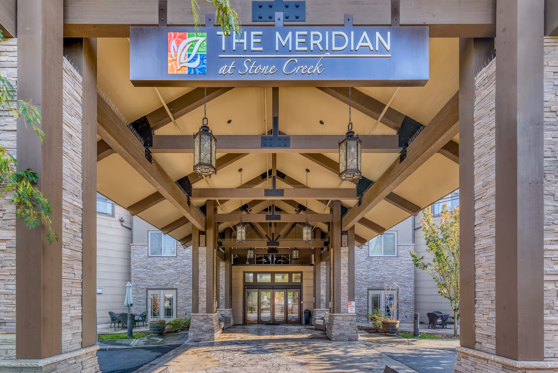 Covered entrance canopy with hanging lanterns and a sign reading 'The Meridian at Stone Creek' over the driveway.
