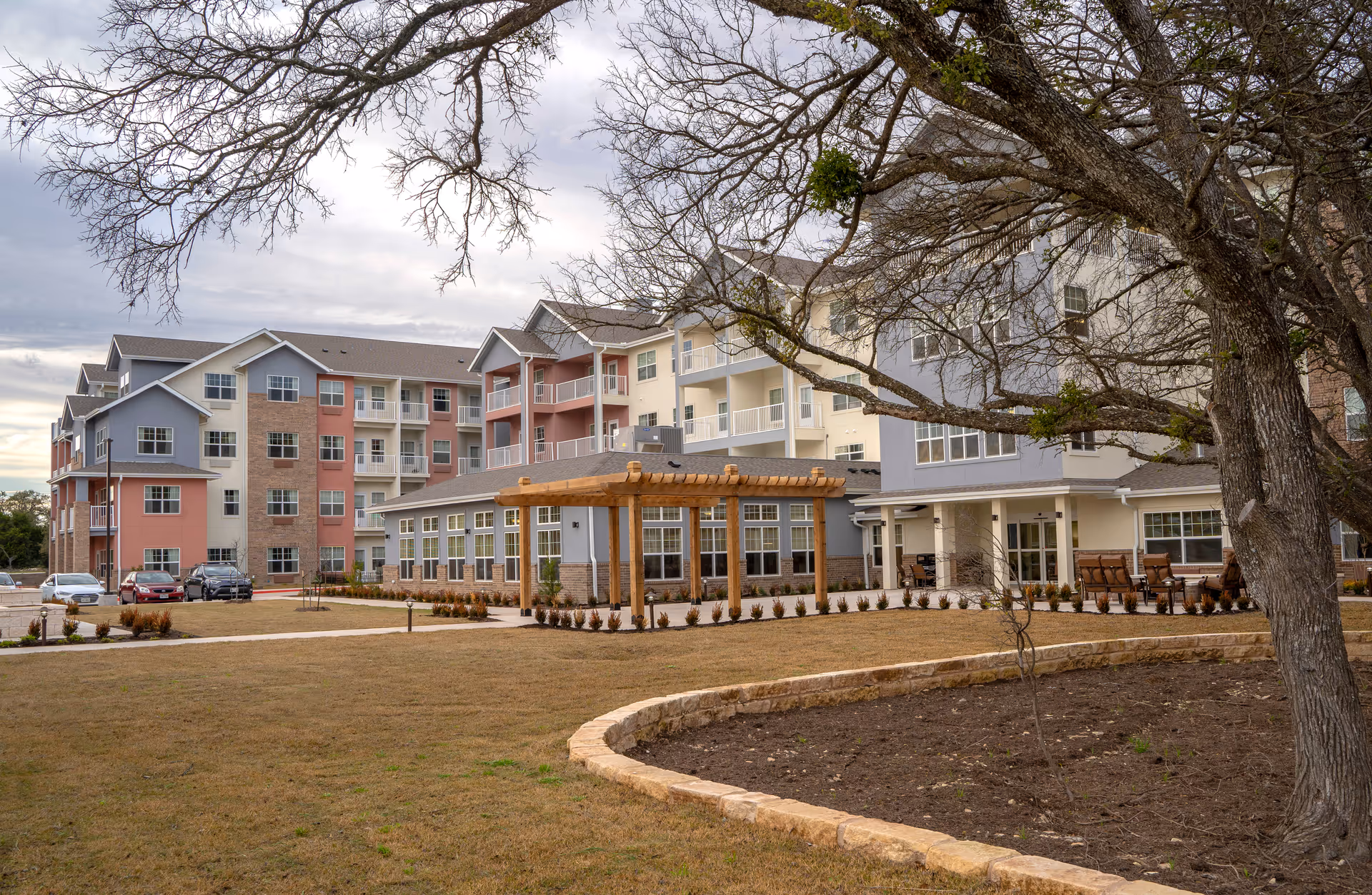 Exterior of a multi-story senior living building with balconies, a wooden pergola, and landscaped front lawn.