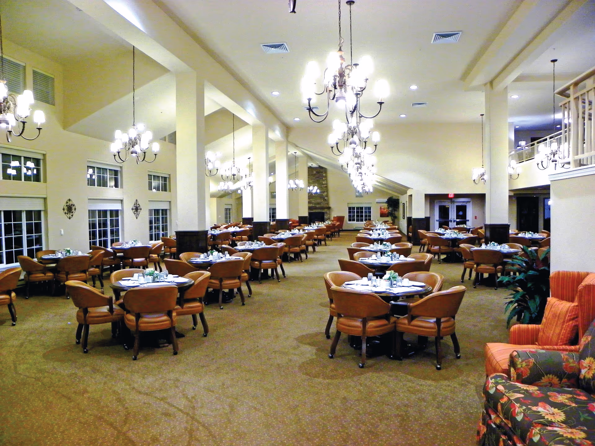 Spacious dining room with multiple round tables, leather chairs, and chandeliers set for meals.
