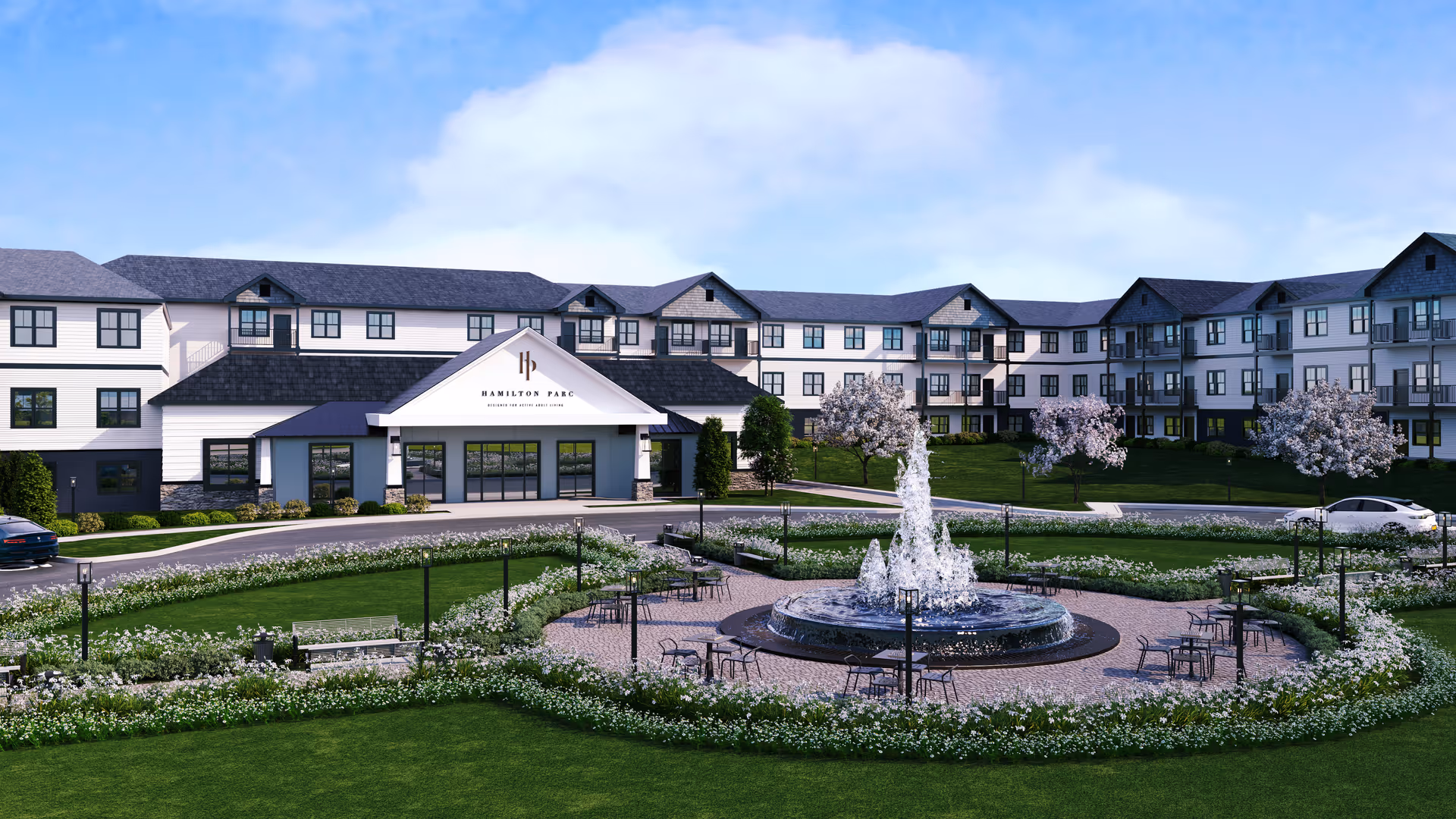 Front exterior of the Hamilton Parc senior living building with a landscaped circular fountain and seating area in the foreground.