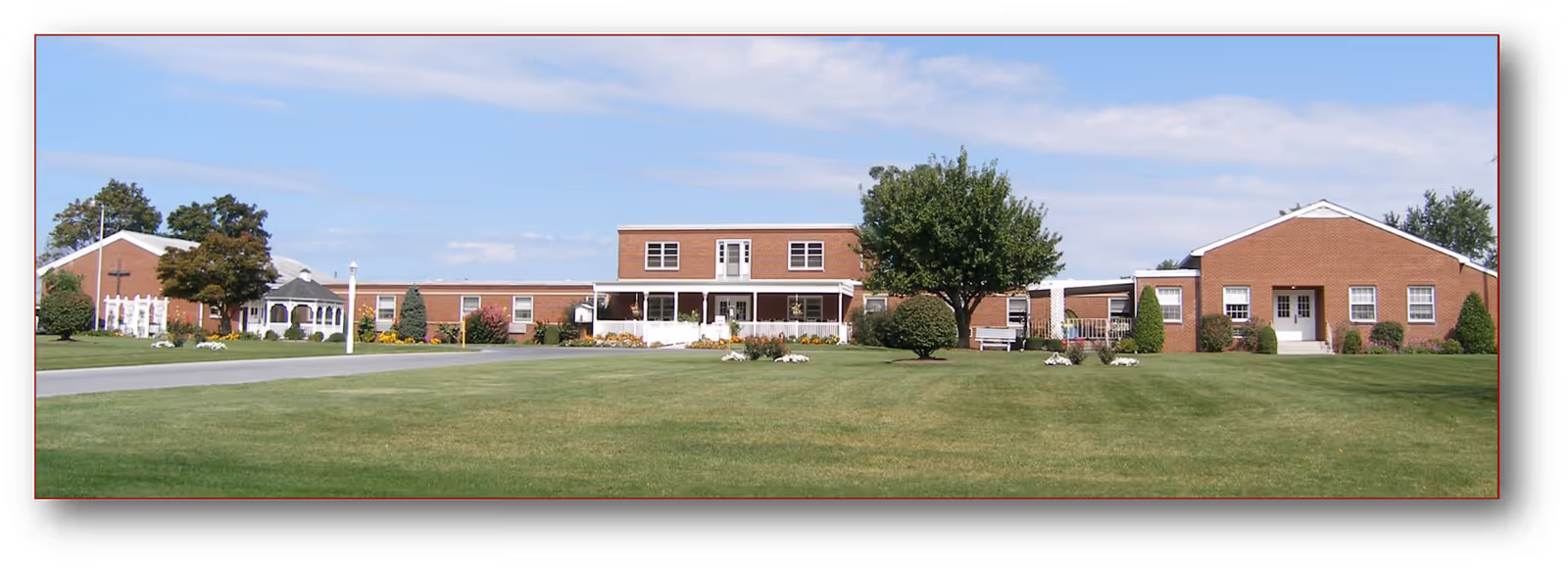 Wide exterior view of Countryside Christian Community showing a large, single-story brick building with a central two-story section, surrounded by well-maintained green lawn, trees, and shrubs under a partly cloudy sky.