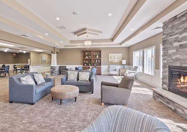 Spacious senior living lounge with blue sofas, a stone fireplace, and large windows.