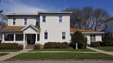 Two-story white building with a covered front entrance and trimmed shrubs.